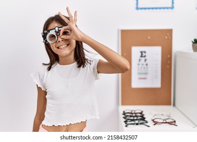 Young Hispanic Girl Wearing Optometry Glasses Smiling Happy Doing Ok Sign With Hand On Eye Looking Through Fingers 