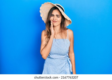 Young Hispanic Girl Wearing Summer Hat Touching Mouth With Hand With Painful Expression Because Of Toothache Or Dental Illness On Teeth. Dentist 