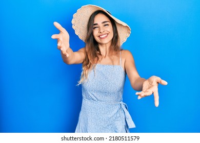 Young hispanic girl wearing summer hat looking at the camera smiling with open arms for hug. cheerful expression embracing happiness. 
