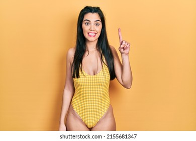 Young hispanic girl wearing swimsuit showing and pointing up with finger number one while smiling confident and happy. 