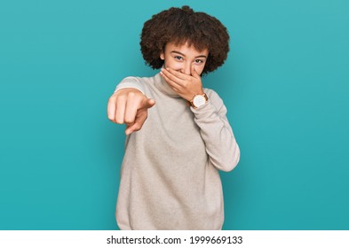 Young Hispanic Girl Wearing Wool Winter Sweater Laughing At You, Pointing Finger To The Camera With Hand Over Mouth, Shame Expression 