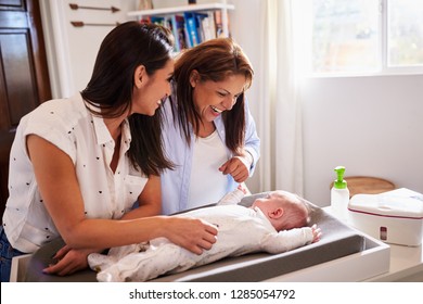 Young Hispanic Grandmother And Adult Daughter Playing With Her Baby Son On Changing Table, Waist Up