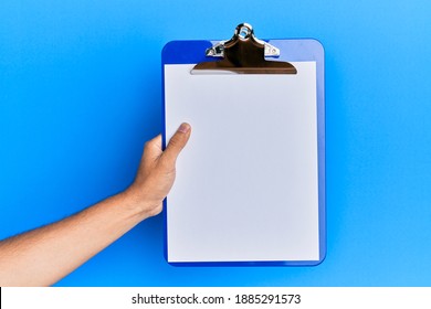 Young hispanic hand holding clipboard over isolated blue background.