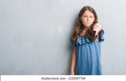 Young Hispanic Kid Over Grunge Grey Wall Looking Unhappy And Angry Showing Rejection And Negative With Thumbs Down Gesture. Bad Expression.