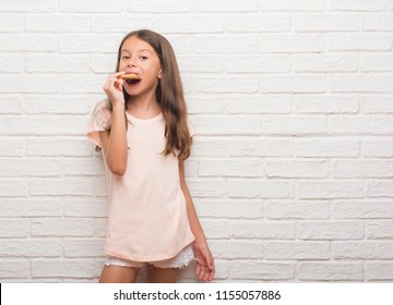 Young Hispanic Kid Over White Brick Wall Eating Chocolate Chips Cooky With A Confident Expression On Smart Face Thinking Serious