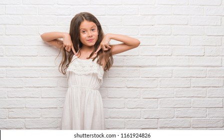 Young Hispanic Kid Over White Brick Wall Looking Confident With Smile On Face, Pointing Oneself With Fingers Proud And Happy.