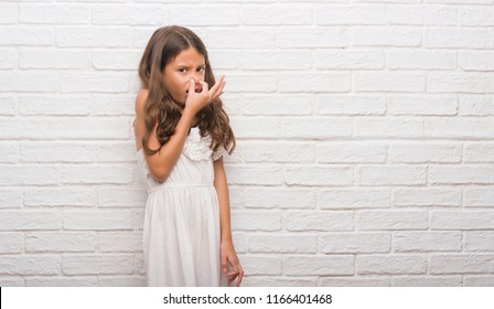 Young Hispanic Kid Over White Brick Wall Smelling Something Stinky And Disgusting, Intolerable Smell, Holding Breath With Fingers On Nose. Bad Smells Concept.