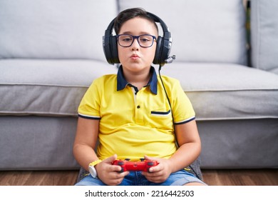 Young Hispanic Kid Playing Video Game Holding Controller Wearing Headphones Looking At The Camera Blowing A Kiss On Air Being Lovely And Sexy. Love Expression. 