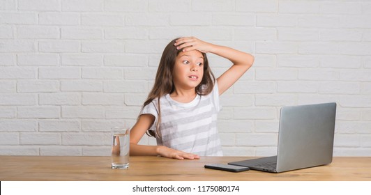 Young Hispanic Kid Sitting On The Table Using Computer Laptop Stressed With Hand On Head, Shocked With Shame And Surprise Face, Angry And Frustrated. Fear And Upset For Mistake.