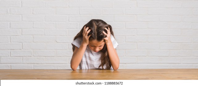 Young Hispanic Kid Sitting On The Table At Home Suffering From Headache Desperate And Stressed Because Pain And Migraine. Hands On Head.