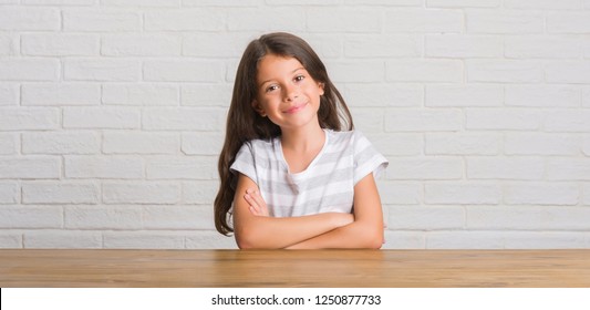 Young Hispanic Kid Sitting On The Table At Home Happy Face Smiling With Crossed Arms Looking At The Camera. Positive Person.