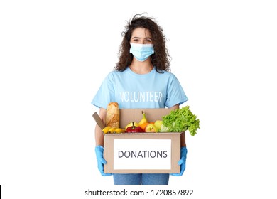 Young Hispanic Latin Woman Courier Wears Volunteer Tshirt, Medical Face Mask, Gloves Look At Camera Holding Donations Box Delivering Food Delivery Stand Isolated On White Studio Background. Portrait.