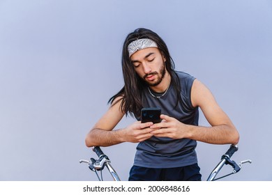 young hispanic latino man with long hair using his smart cell phone riding a bicycle, looking for a solution - Powered by Shutterstock