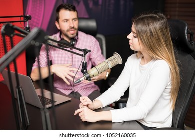 Young Hispanic Male And Female Host Moderating A Live Radio Show At Radio Station