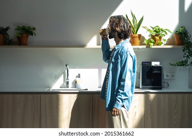 Young hispanic male worker drinking coffee from paper cup in coworking space kitchen. Coffee break at the office. Pause. Sunbeam. Copy space. Co working office concept.