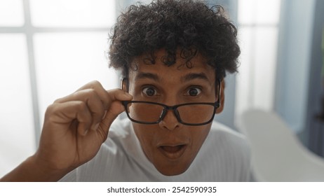 Young hispanic man adjusting glasses in an office setting with surprised expression - Powered by Shutterstock