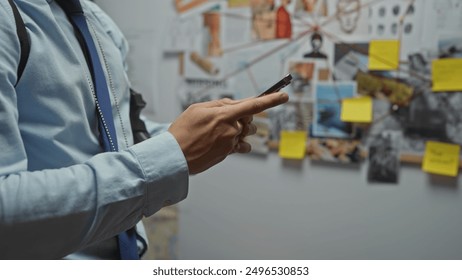 A young hispanic man analyzes evidence at a detective's office using a mobile phone - Powered by Shutterstock