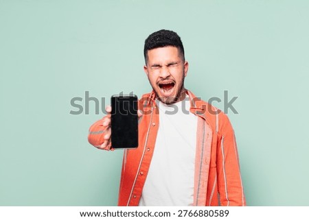 young hispanic man angry expression and holding a mobile phone