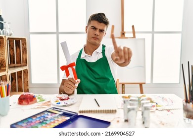 Young Hispanic Man At Art Studio Holding Degree Pointing With Finger Up And Angry Expression, Showing No Gesture 