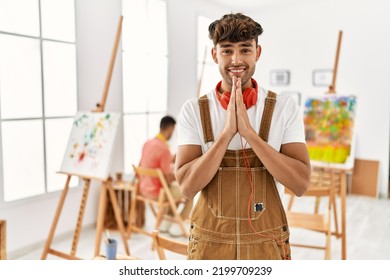 Young Hispanic Man At Art Studio Praying With Hands Together Asking For Forgiveness Smiling Confident. 