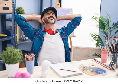 Young hispanic man artist relaxed and hands head sitting table at art studio