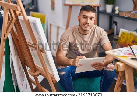 Young hispanic man artist smiling confident drawing on notebook at art studio