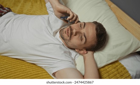 A young hispanic man with a beard lies on a bed in his bedroom, talking on the phone and relaxing in a home setting. - Powered by Shutterstock