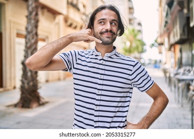 Young hispanic man with beard outdoors at the city smiling doing phone gesture with hand and fingers like talking on the telephone. communicating concepts. 