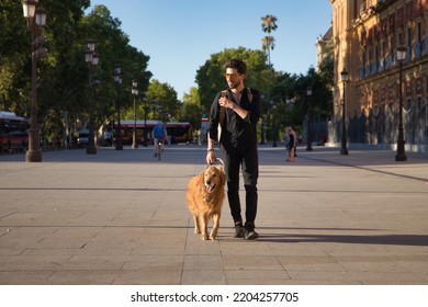 Young Hispanic Man With A Beard, Sunglasses, Black Shirt And Backpack, Walking Around The City With His Dog. Concept Animals, Dogs, Love, Pets, Golden.