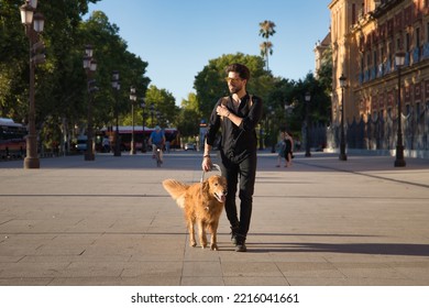 Young Hispanic Man With A Beard, Sunglasses, Black Shirt And Backpack, Walking Around The City With His Dog. Concept Animals, Dogs, Love, Pets, Golden.