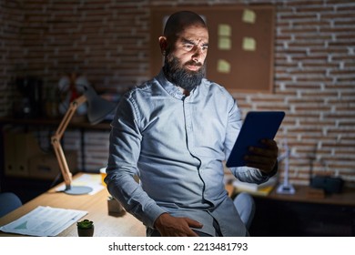 Young hispanic man with beard and tattoos working at the office at night skeptic and nervous, frowning upset because of problem. negative person.  - Shutterstock ID 2213481793
