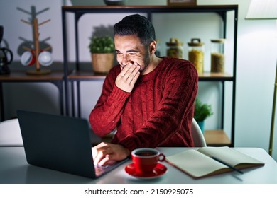 Young Hispanic Man With Beard Using Computer Laptop At Night At Home Laughing And Embarrassed Giggle Covering Mouth With Hands, Gossip And Scandal Concept 