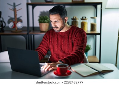 Young hispanic man with beard using computer laptop at night at home skeptic and nervous, frowning upset because of problem. negative person.  - Shutterstock ID 2282432799