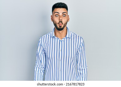 Young hispanic man with beard wearing casual striped shirt making fish face with lips, crazy and comical gesture. funny expression. 