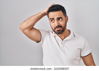 Young hispanic man with beard wearing casual clothes over white background confuse and wondering about question. uncertain with doubt, thinking with hand on head. pensive concept.  - Powered by Shutterstock