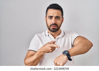 Young hispanic man with beard wearing casual clothes over white background in hurry pointing to watch time, impatience, upset and angry for deadline delay  - Shutterstock ID 2213498749