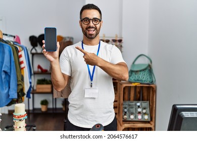 Young Hispanic Man With Beard Working As Manager At Retail Boutique Holding Smartphone Smiling Happy Pointing With Hand And Finger 