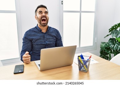 Young hispanic man with beard working at the office with laptop angry and mad screaming frustrated and furious, shouting with anger. rage and aggressive concept.  - Shutterstock ID 2140265045