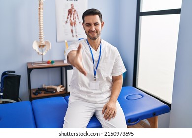 Young hispanic man with beard working at pain recovery clinic smiling friendly offering handshake as greeting and welcoming. successful business.  - Powered by Shutterstock