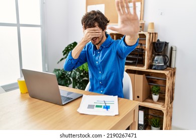 Young Hispanic Man With Beard Working At The Office Using Computer Laptop Covering Eyes With Hands And Doing Stop Gesture With Sad And Fear Expression. Embarrassed And Negative Concept. 