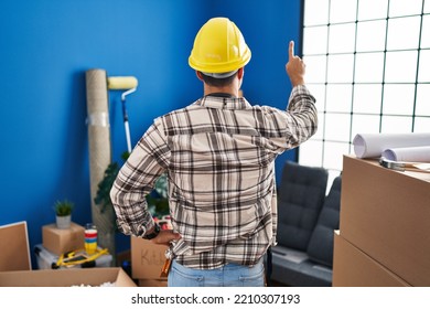 Young Hispanic Man With Beard Working At Home Renovation Posing Backwards Pointing Ahead With Finger Hand 