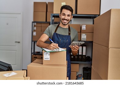 Young hispanic man business worker writing on clipboard holding dollars at storehouse - Shutterstock ID 2181643685