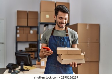 Young hispanic man business worker using smartphone holding packages at storehouse - Shutterstock ID 2190156289