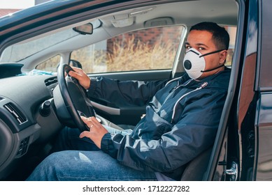 Young Hispanic Man Is In The Car Wears Protective Mask To Prevent The Spread Of Coronavirus. Young Hispanic Taxi Driver Wearing A Protective Mask And Waiting For A Client. Covid 19. Coronavirus.