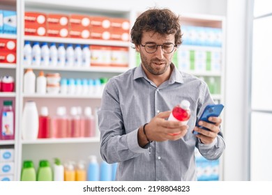 Young Hispanic Man Customer Using Smartphone Holding Medicine Bottle At Pharmacy