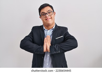 Young hispanic man with down syndrome wearing business style praying with hands together asking for forgiveness smiling confident.  - Shutterstock ID 2230654445
