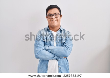 Young hispanic man with down syndrome wearing casual denim jacket over white background happy face smiling with crossed arms looking at the camera. positive person. 