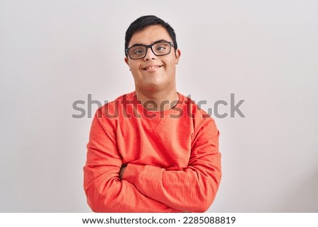 Young hispanic man with down syndrome standing over white background happy face smiling with crossed arms looking at the camera. positive person. 