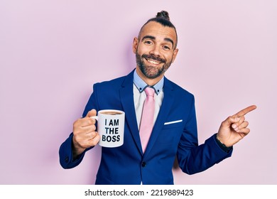 Young Hispanic Man Drinking From I Am The Boss Coffee Cup Smiling Happy Pointing With Hand And Finger To The Side 