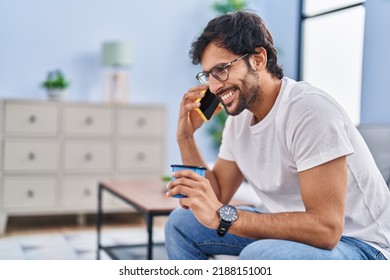 Young Hispanic Man Drinking Coffee And Talking On The Smartphone At Home